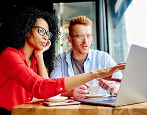 Businesswoman in glasses pointing finger on laptop screen and discussing work with colleague