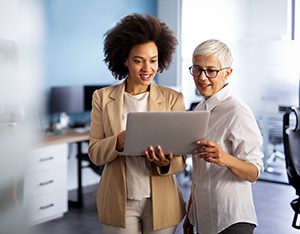 Smiling business women working together online on a laptop in office